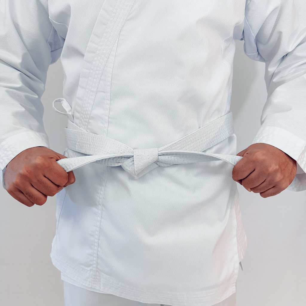 Person wearing a white martial arts uniform with a belt on a plain background