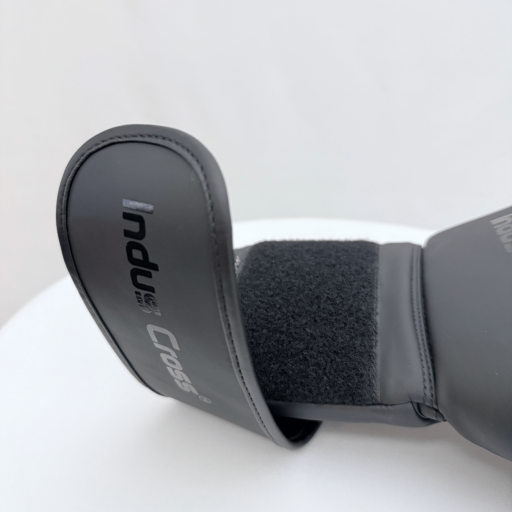 Close-up of a black boxing glove's wrist strap with 'Indus Cross' branding on a white background