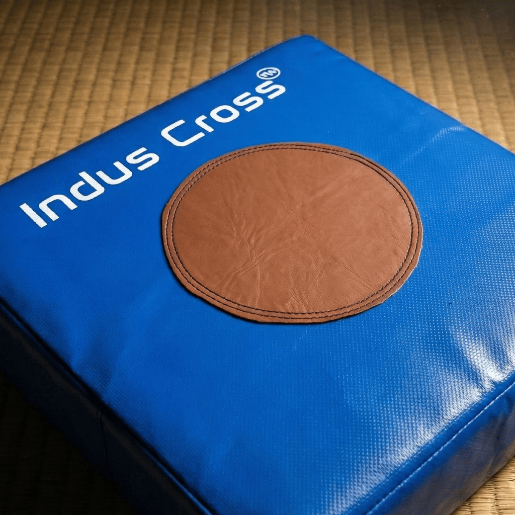 Blue Indus Cross Karate Punching Square Impact Shield with a brown circular patch and 'Indus Cross' branding on a textured surface.