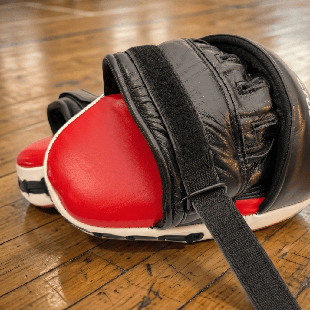 Red and black Indus Cross Ventus-GL Boxing Focus Mitts on a wooden floor.