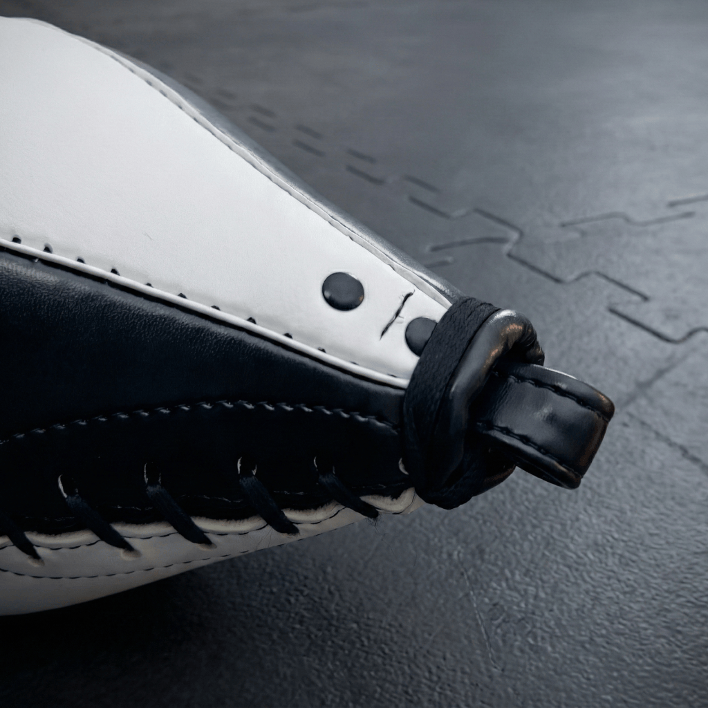 Close-up of a black and white Indus Cross Elite Boxing Speed Bag - Genuine Leather with black stitching on a dark textured surface.