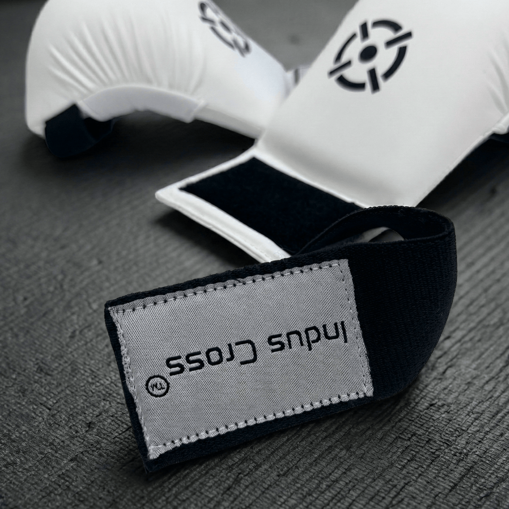 White Indus Cross AeroStrike Karate Glove with a black strap featuring 'Indus Cross' branding on a gray surface.