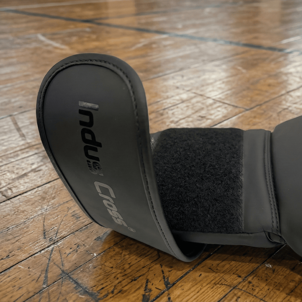 Black Indus Cross Apex-1 Boxing Training Gloves - Artificial Leather on a wooden floor with 'Indus Cross' branding on the wrist strap.