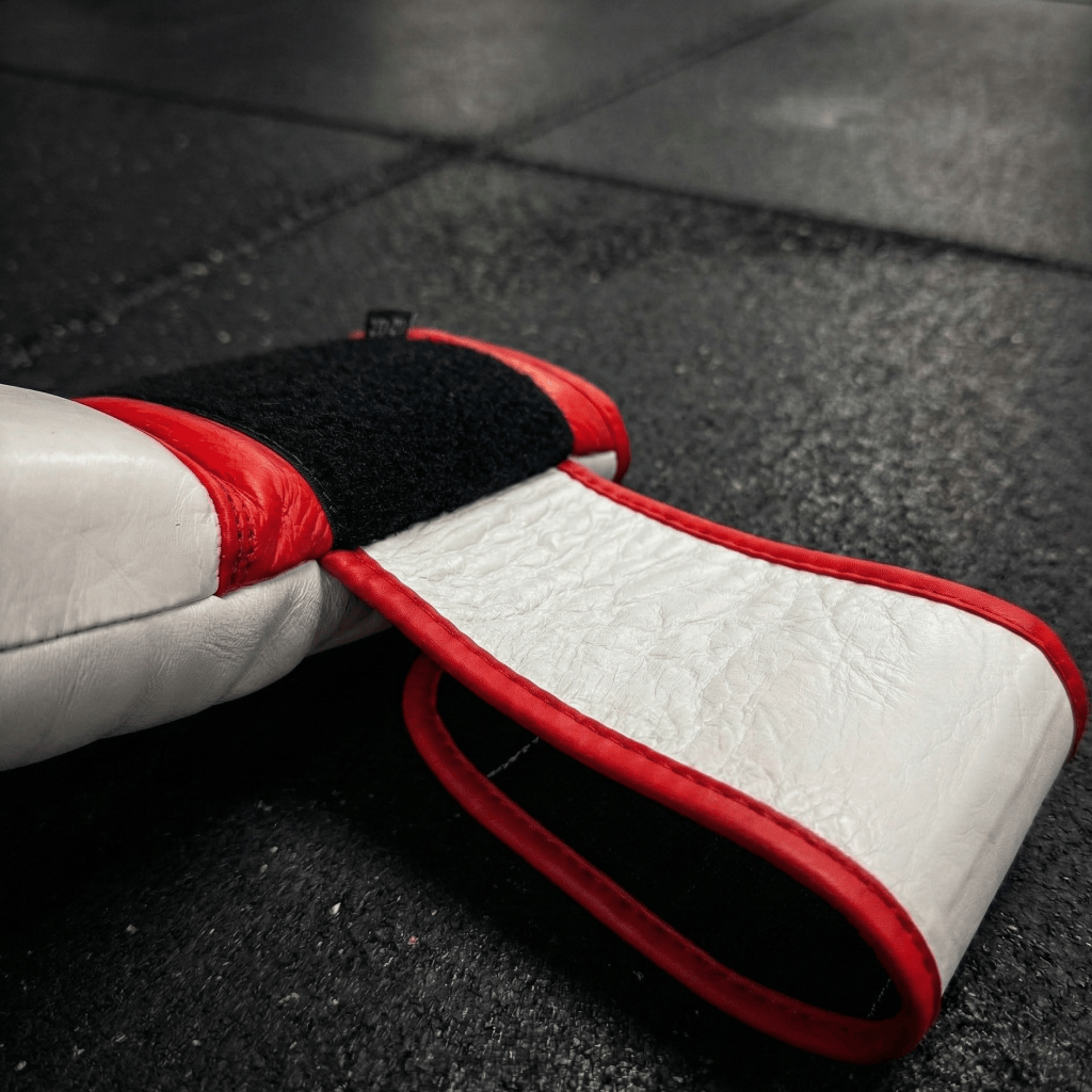 Close-up of a red and white Indus Cross Vertex Boxing Training Gloves - Genuine Leather showing the wrist strap from the outside on a dark textured surface.