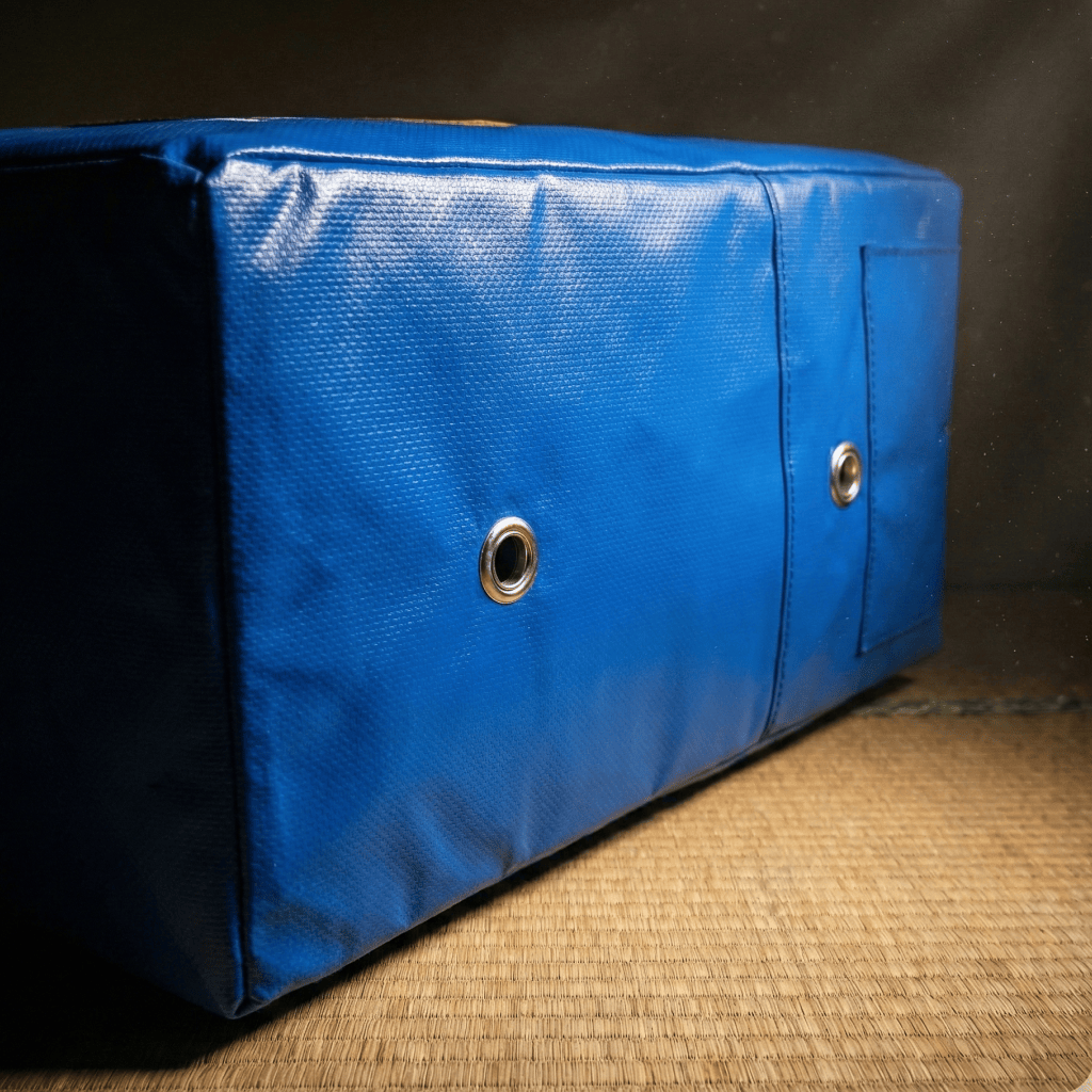 Blue Indus Cross Karate Punching Square Impact Shield with two metal holes for air circulation on a wooden surface.