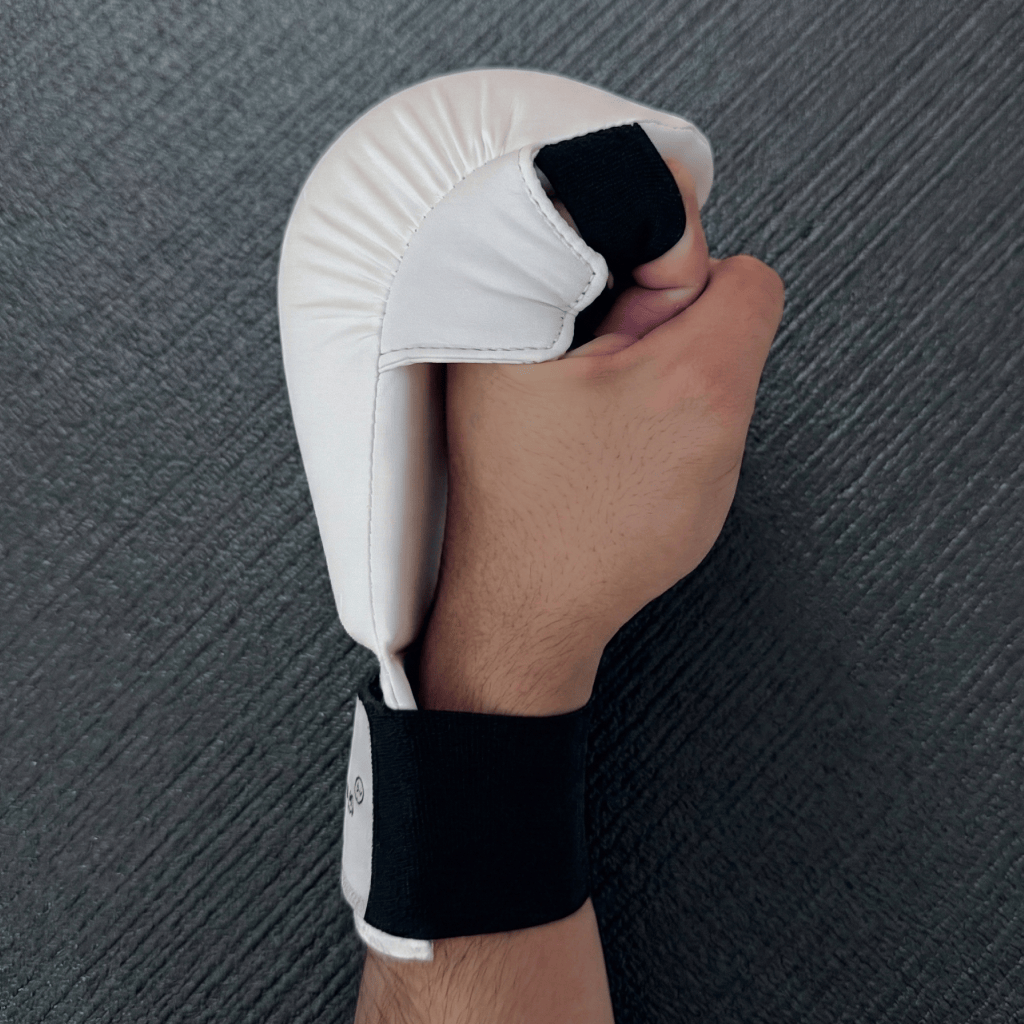 A hand wearing a white Indus Cross AeroStrike Karate Glove from the side  on a dark surface.
