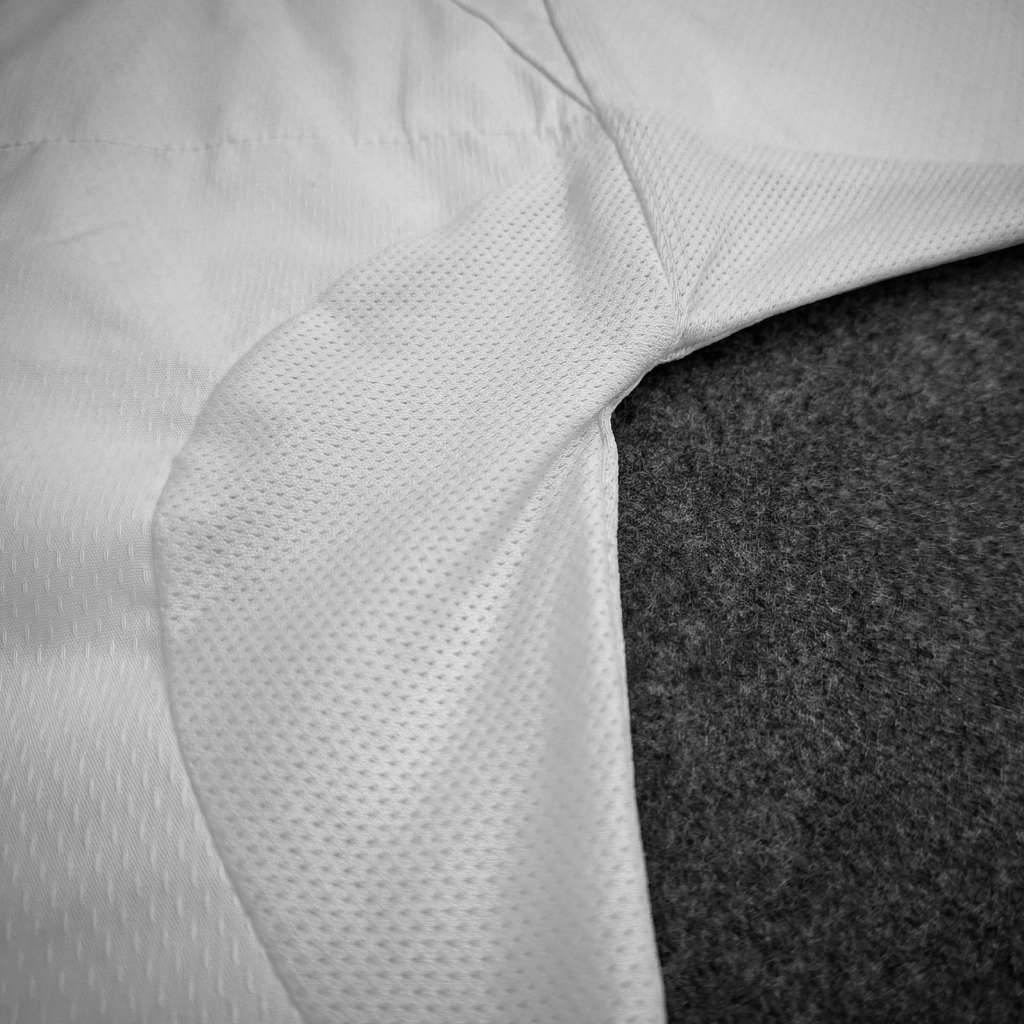 Close-up of a white Indus Cross Lightweight Karate Suit (White Belt Included) with a textured pattern on a dark background.