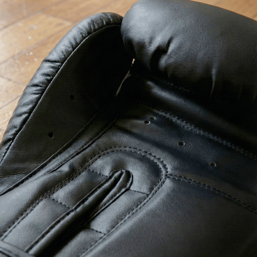 Close-up of a Indus Cross Apex-1 Boxing Training Glove - Artificial Leather glove on a wooden surface.