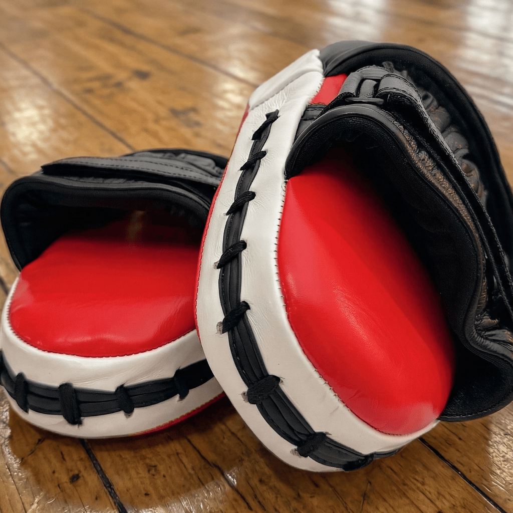 Red and black Indus Cross Ventus-GL Boxing Focus Mitts showing the inside of where the hand is placed on a wooden floor.
