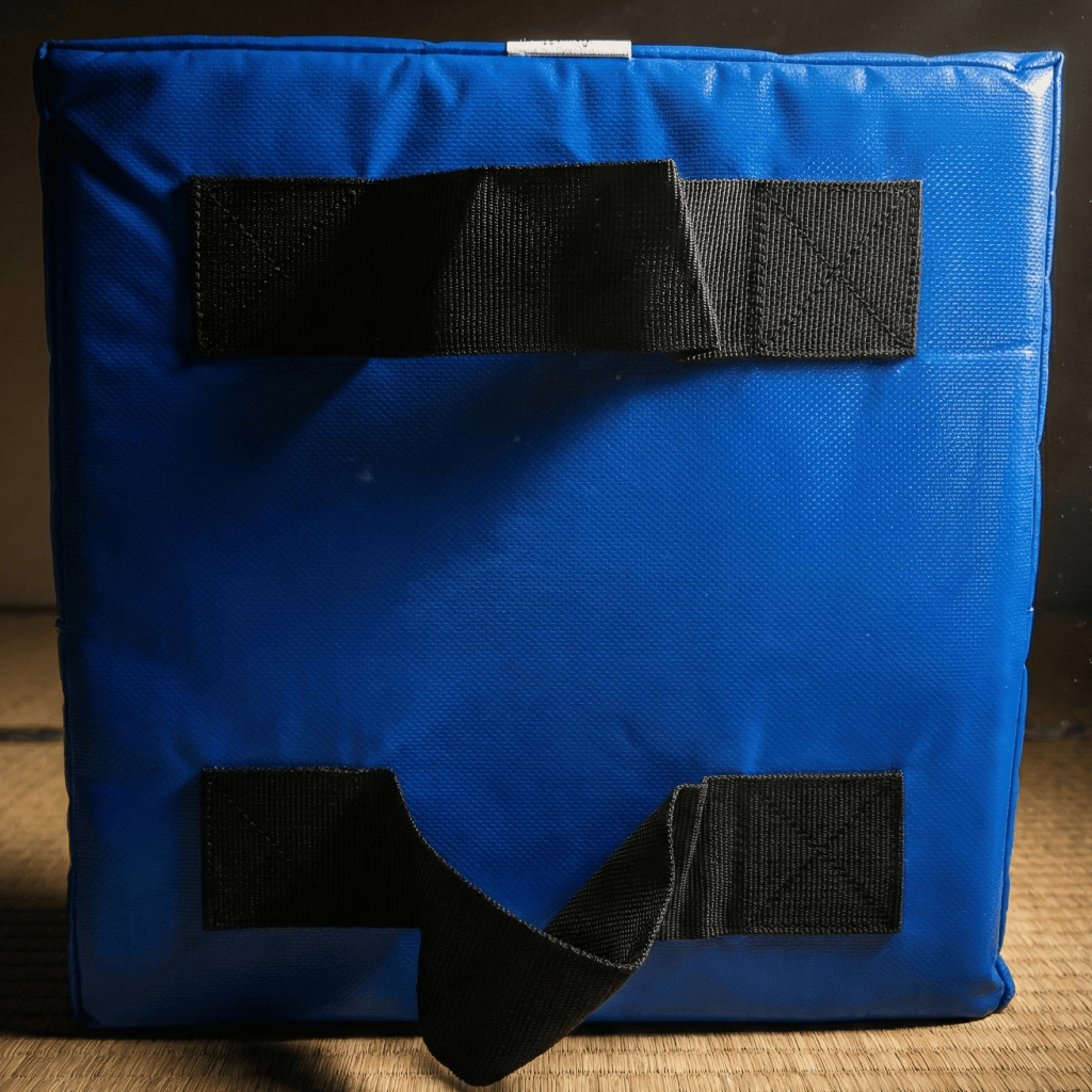 Blue Indus Cross Karate Punching Square Impact Shield with black straps to hold the bag on a wooden surface.