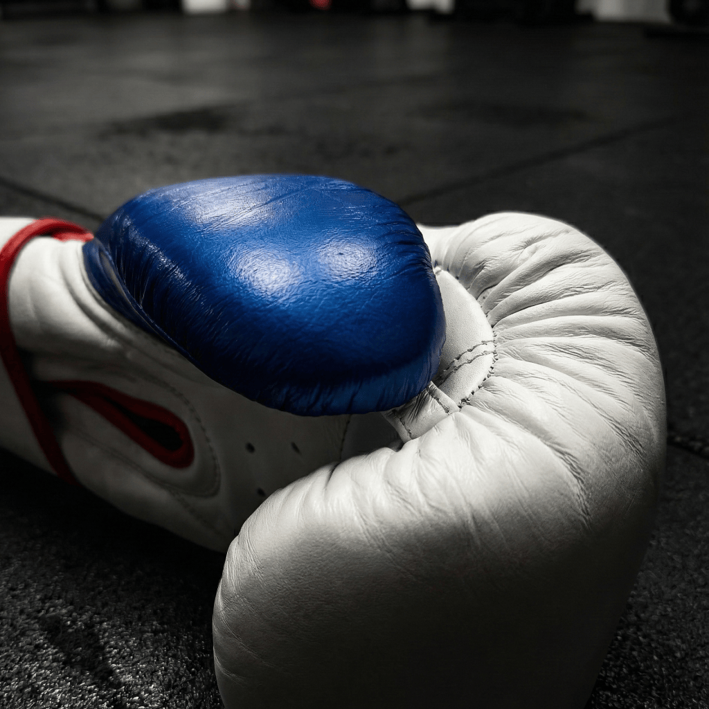 Close-up of a white and blue Indus Cross Vertex Boxing Training Gloves - Genuine Leather on a dark background.