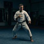 Person in a white martial arts uniform and a white karate body protector with a black belt in a dark dojo.