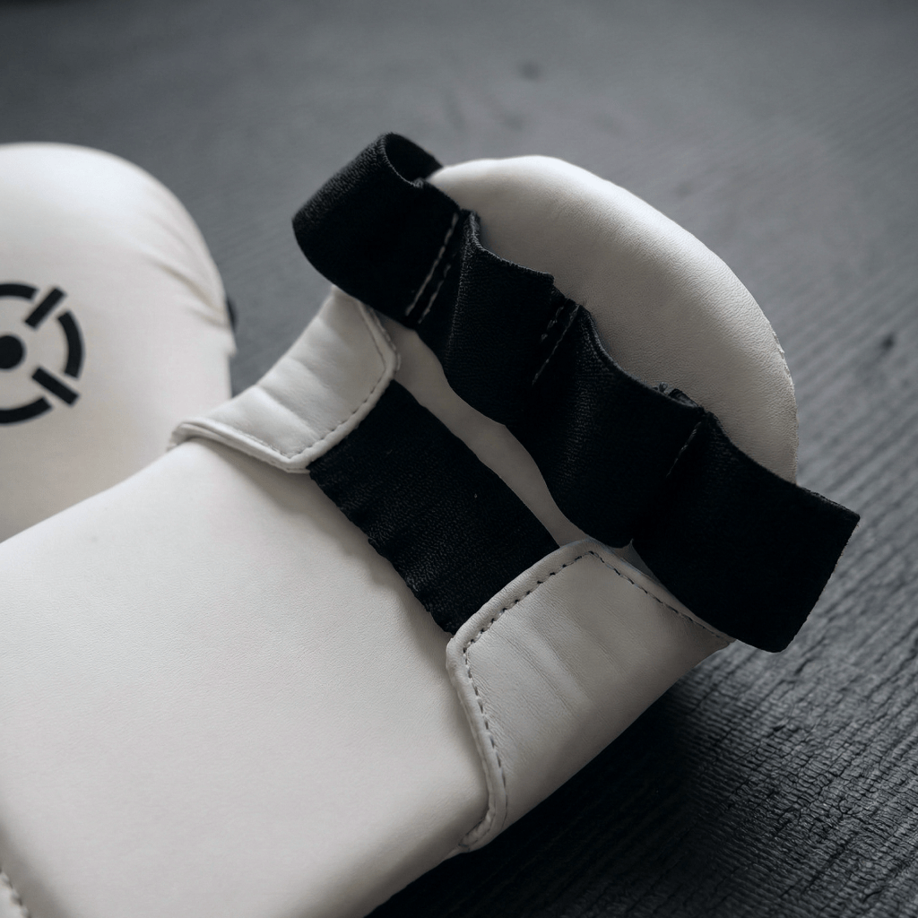 A closeup of a white Indus Cross AeroStrike Karate Glove on a dark surface.