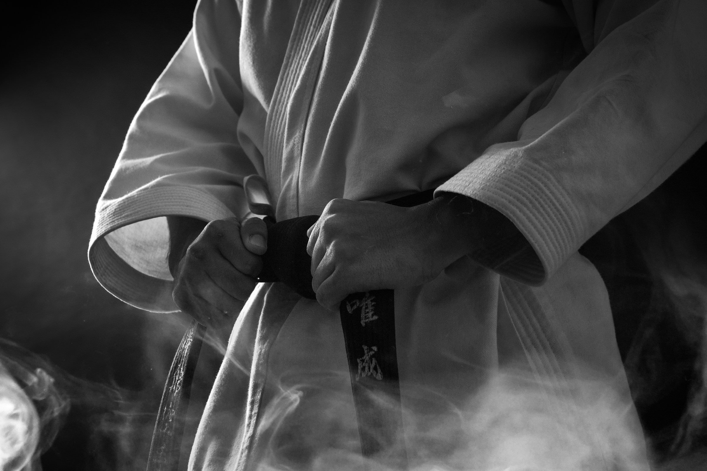 Person in a martial arts uniform holding a belt with smoke in the foreground